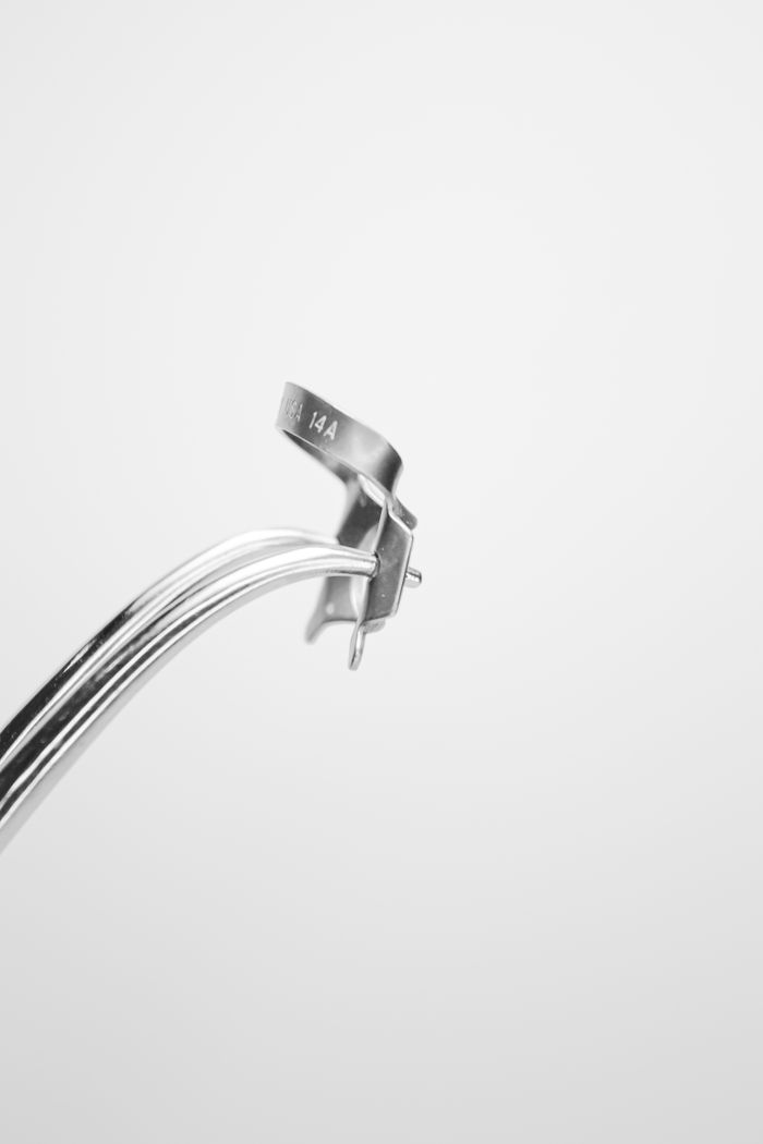 A detailed view of a dental clamp used in dentistry procedures on a plain backdrop.